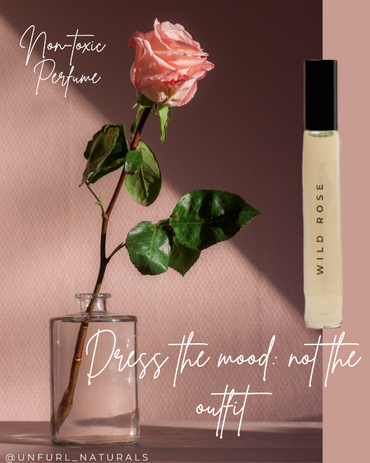 Perfume roller labeled 'Wild Rose' next to a pink rose on a gradient background