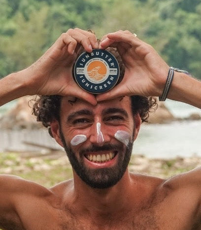 Man smiling with sunscreen on his face holding a tub of sunbutter chemical free sunscreen above his head