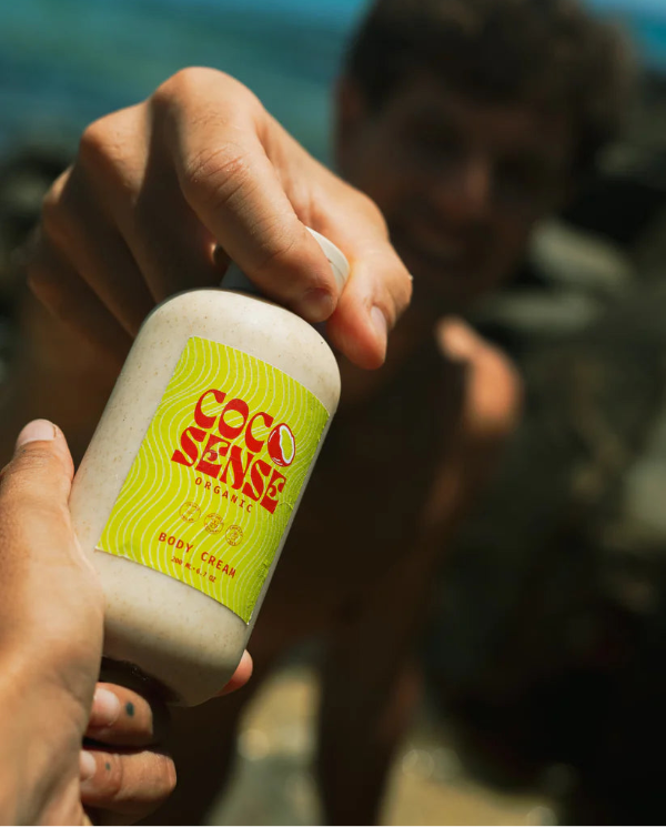 Person holding a jar of 'Coco Sense' organic coconut body cream with a blurred background