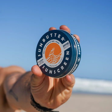 Mans hand holding Sunbutter chemical free sunscreen recyclable tub