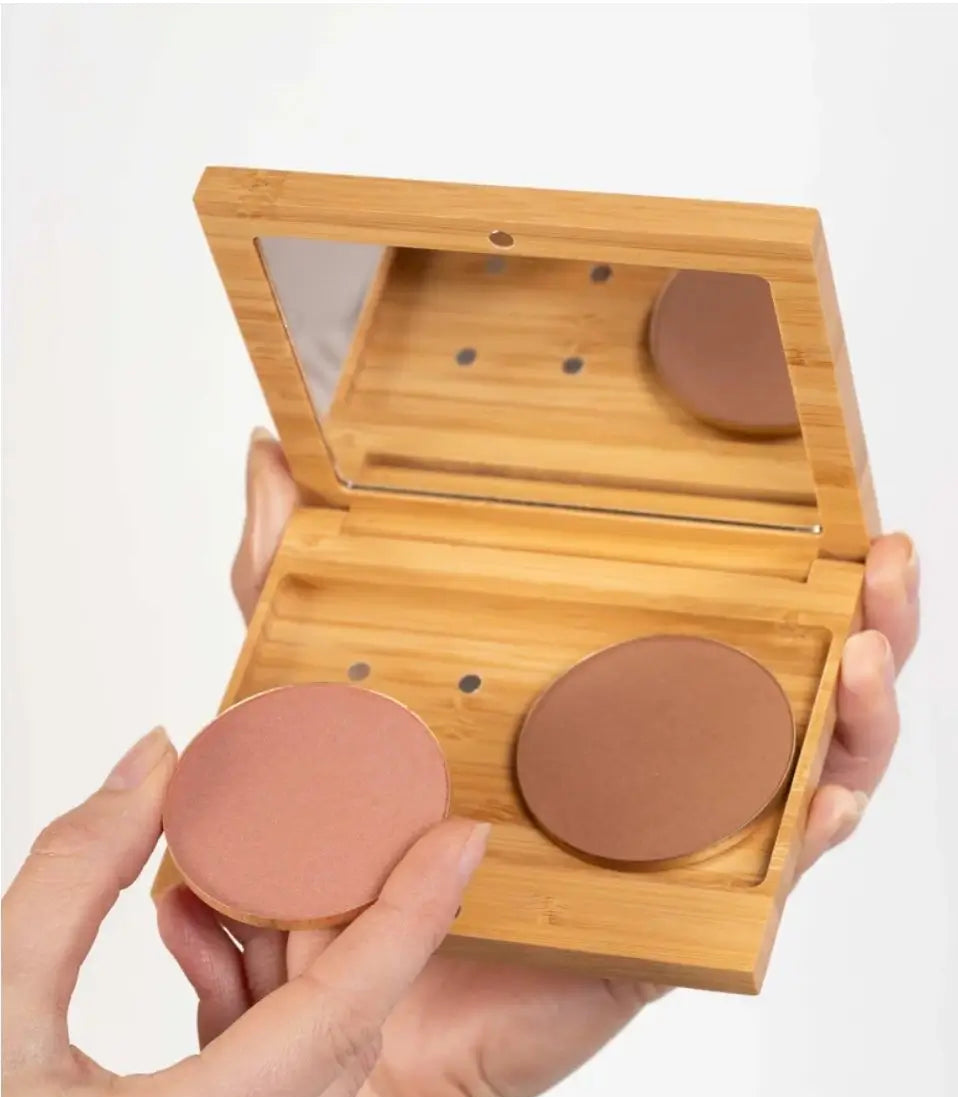 Women's hand holding up a bamboo refillable compact with natural bronzer and blush make-up. 