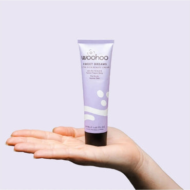 Hand holding a tube of 'woohoo' Sweet Dreams bio-retinol cream against a light purple background