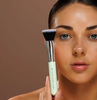 Woman holding an avocado zinc  makeup brush with a neutral background