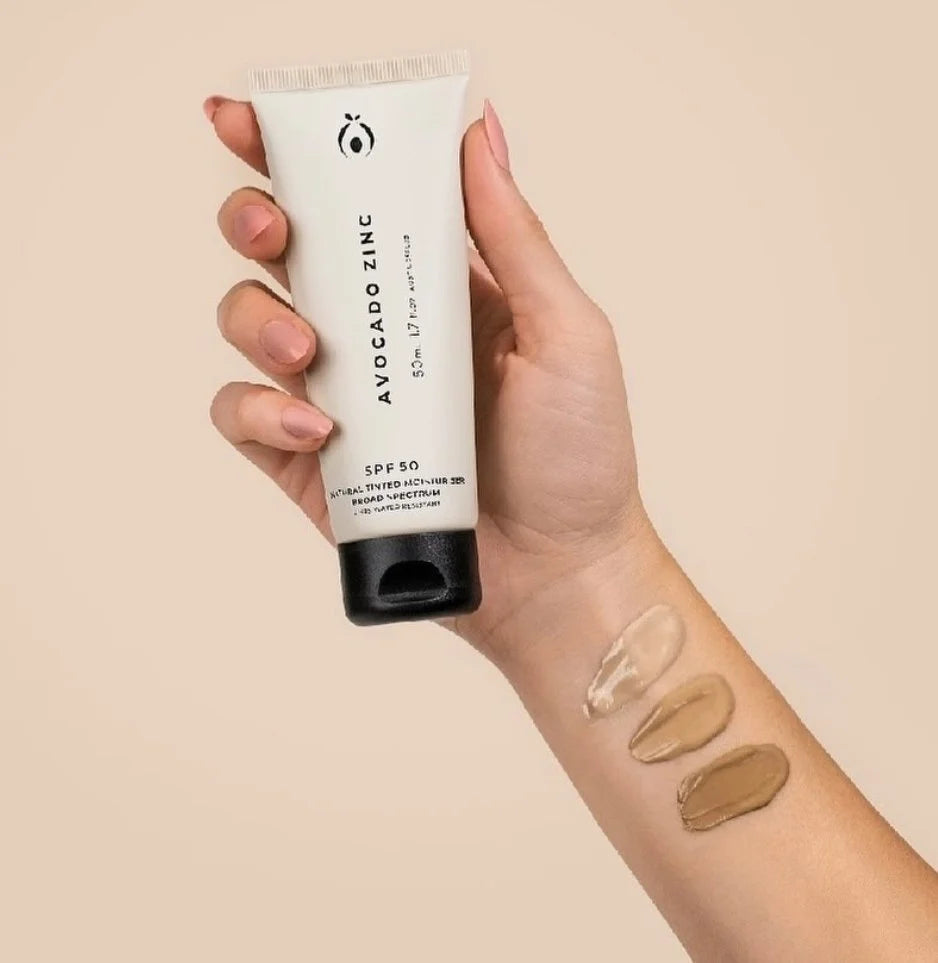 Hand holding a tube of Avocado Zinc sunscreen with swatches on a beige background