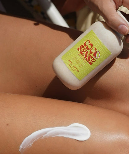 Person applying a white cream labeled coconut body cream onto their leg.