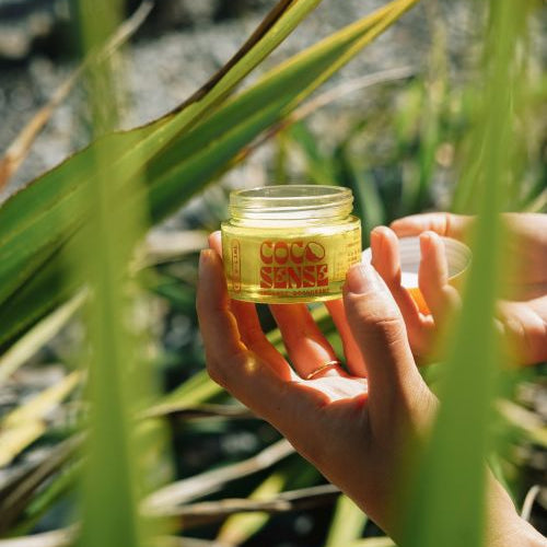 Womans hands holding a jar of open organic deodorant cream against green plants. 