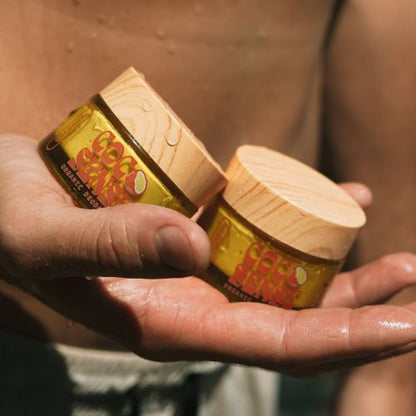 Mans hand holding two jars of cocosense organic coconut deodorant creams. 