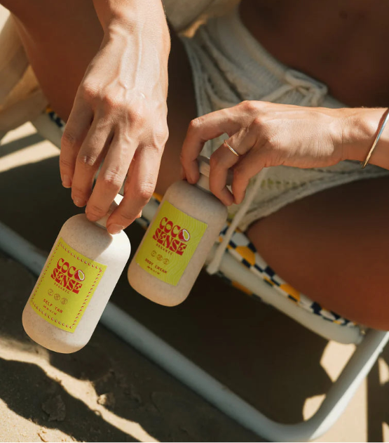 A women holding two bottles of organic Self tan cream on the beach. 