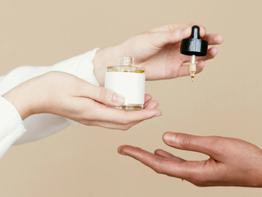 women's hands dropping organic face oil into another women's hand using a dropper.