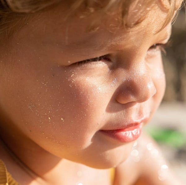 Close-up of a child's face with glitter sunblock on a blurred natural background