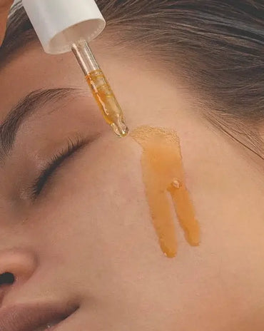 women applying golden face oil to her cheek with a dropper