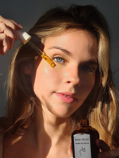 women applying organic face oil to her cheek with a dropper and holding a bottle in the other hand. 