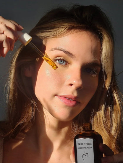 women applying organic face oil to her cheek with a dropper and holding a bottle in the other hand. 