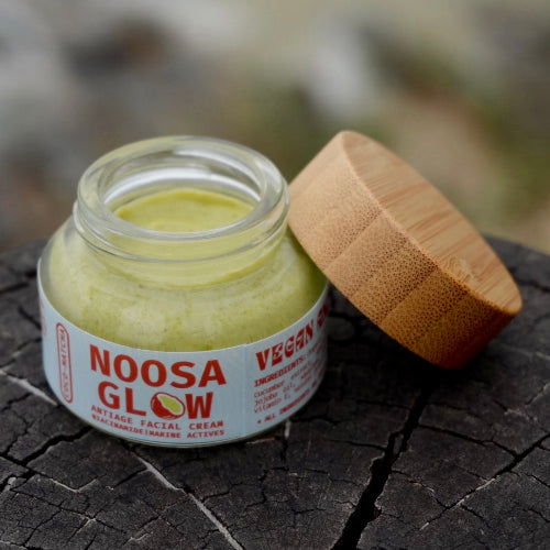 Jar of Noosa Glow anti-aging facial cream on a textured surface with a blurred natural background