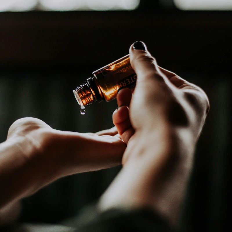 Women's dropping natural skincare oils from a glass bottle into hands. 